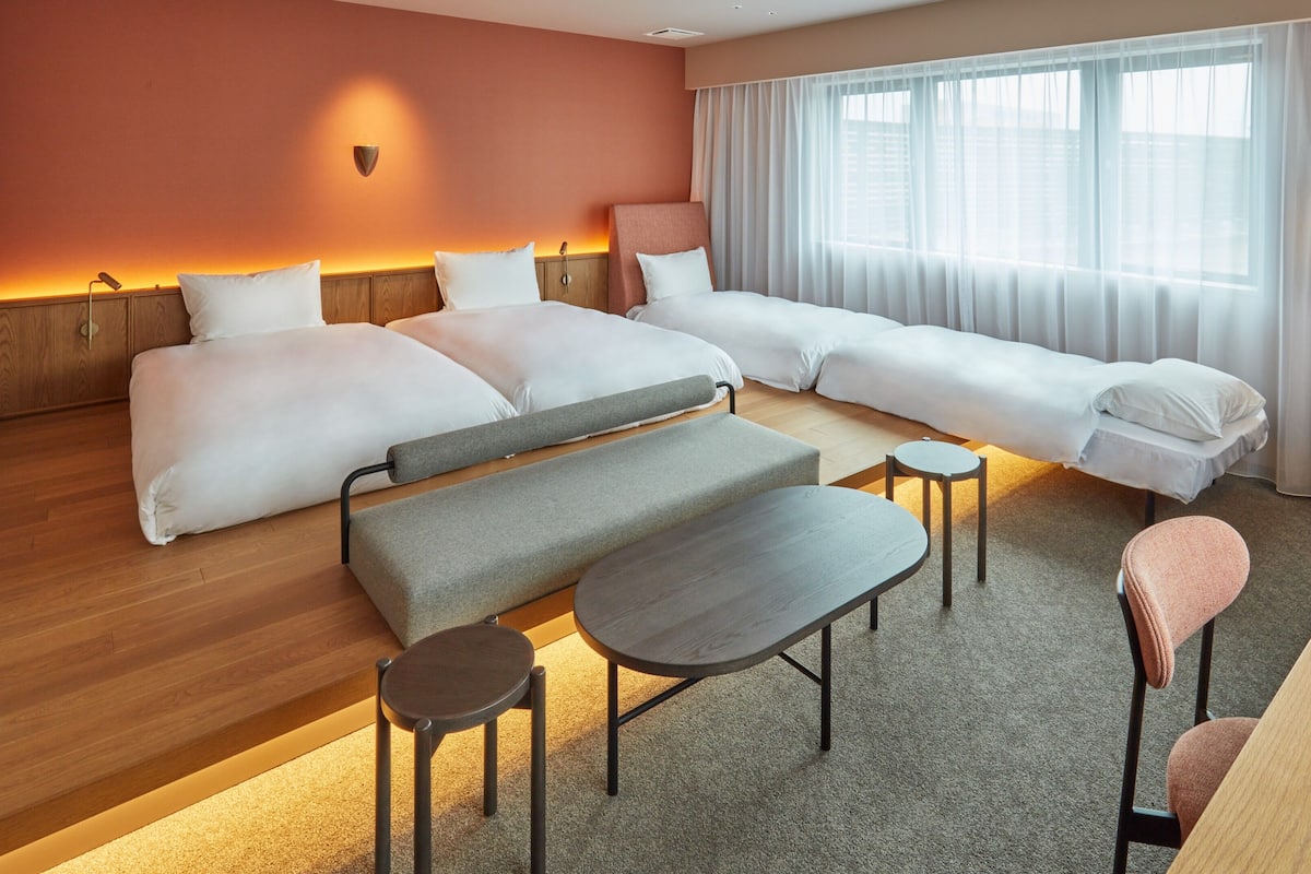 Een hotelkamer met twee bedden, een bank, een tafeltje, een bankje en een lamp.