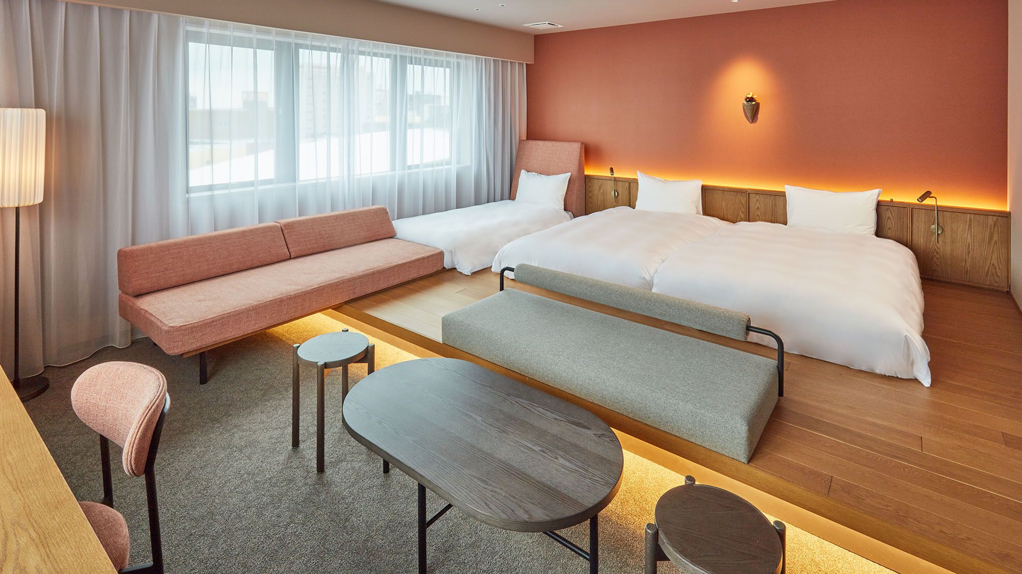 Une chambre d’hôtel avec un canapé, deux lits simples, une petite table, un banc et une lampe.