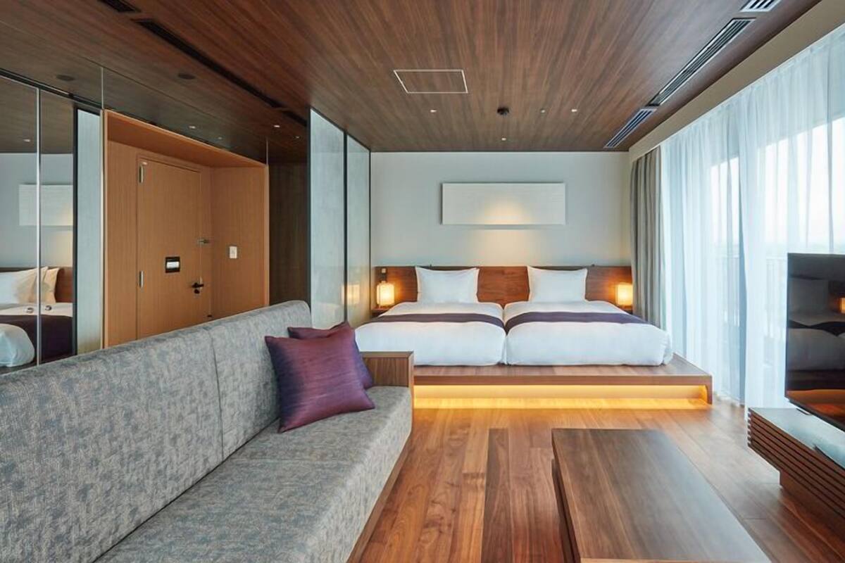 Een moderne hotelkamer met een groot bed, een bank, een televisie en een ruim venster.