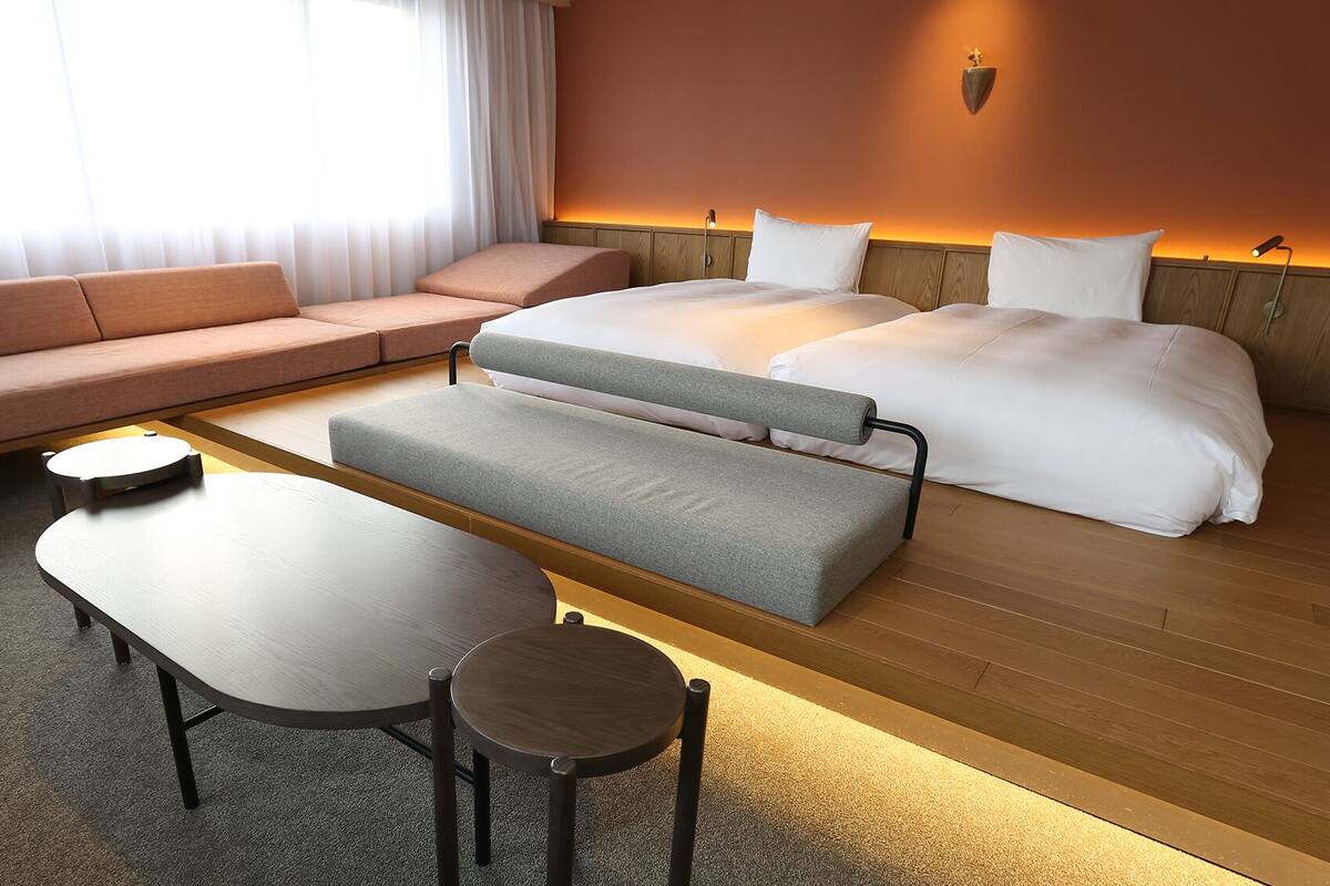 Een hotelkamer met een bank, een bed, een houten bankje, een tafel en een lamp.