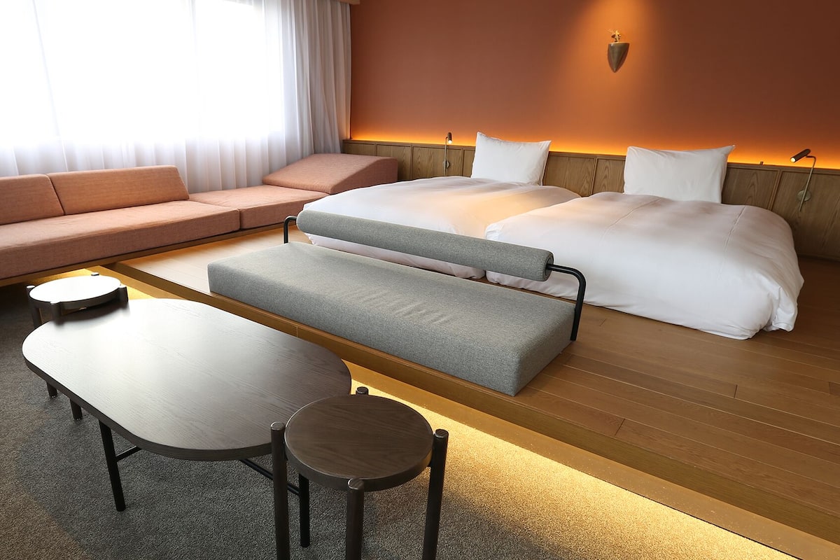 Une chambre d’hôtel avec un canapé, un lit, un banc, une table et une lampe.