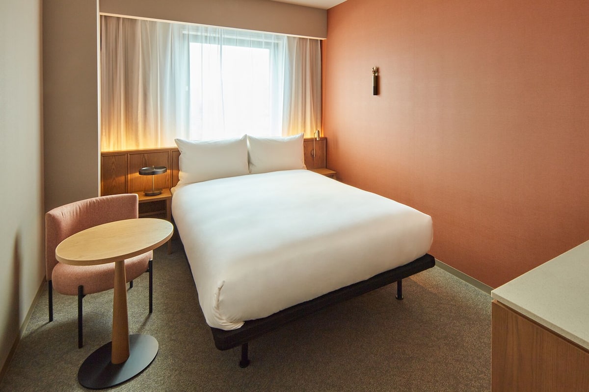 Une chambre d’hôtel avec un lit, un bureau, une chaise et une table de chevet.