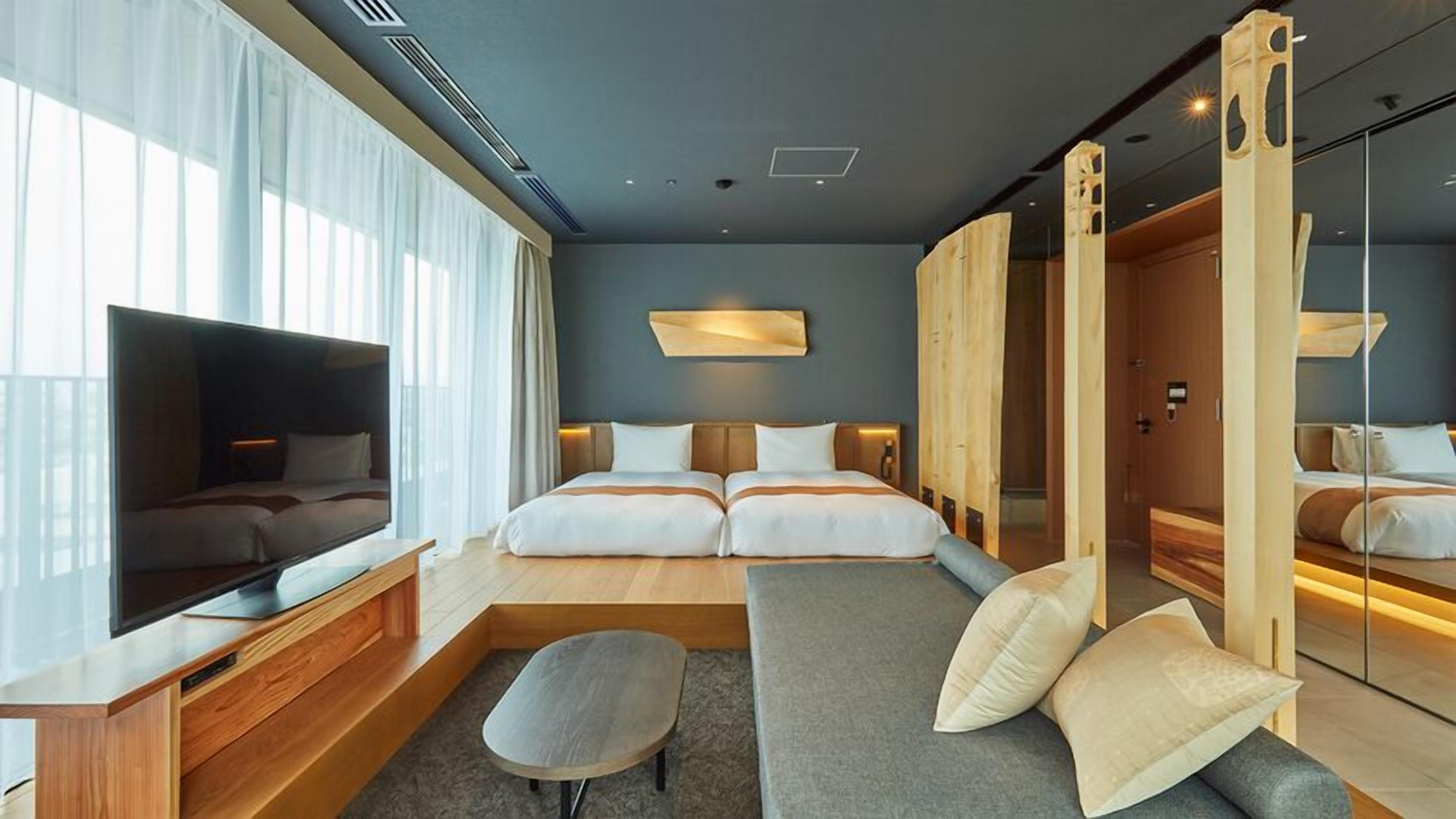 Une chambre d’hôtel moderne avec un grand lit, un canapé, une télévision et une armoire en bois.