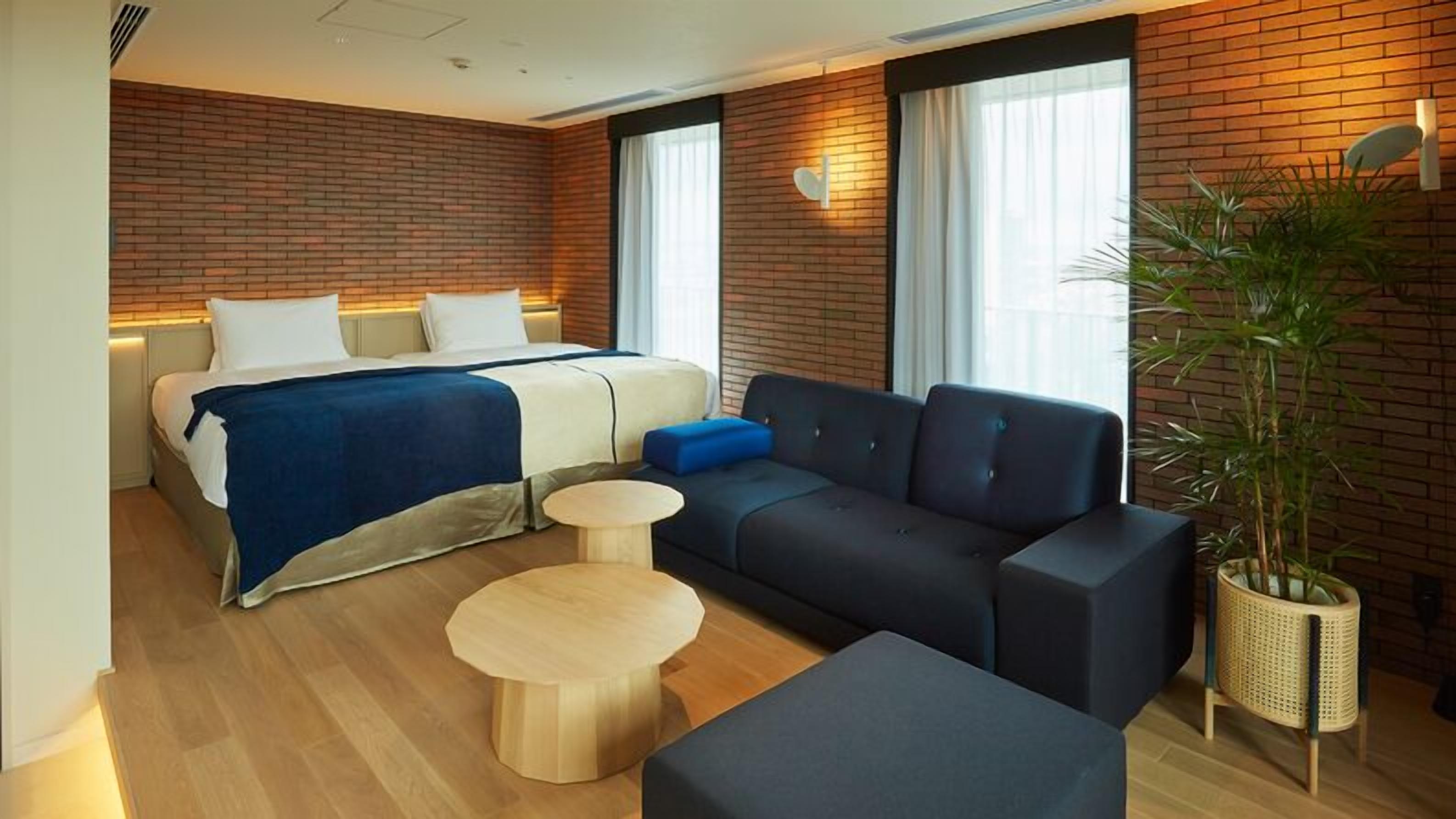 Une chambre d’hôtel moderne avec un lit, un canapé, des tables rondes et une plante en pot.