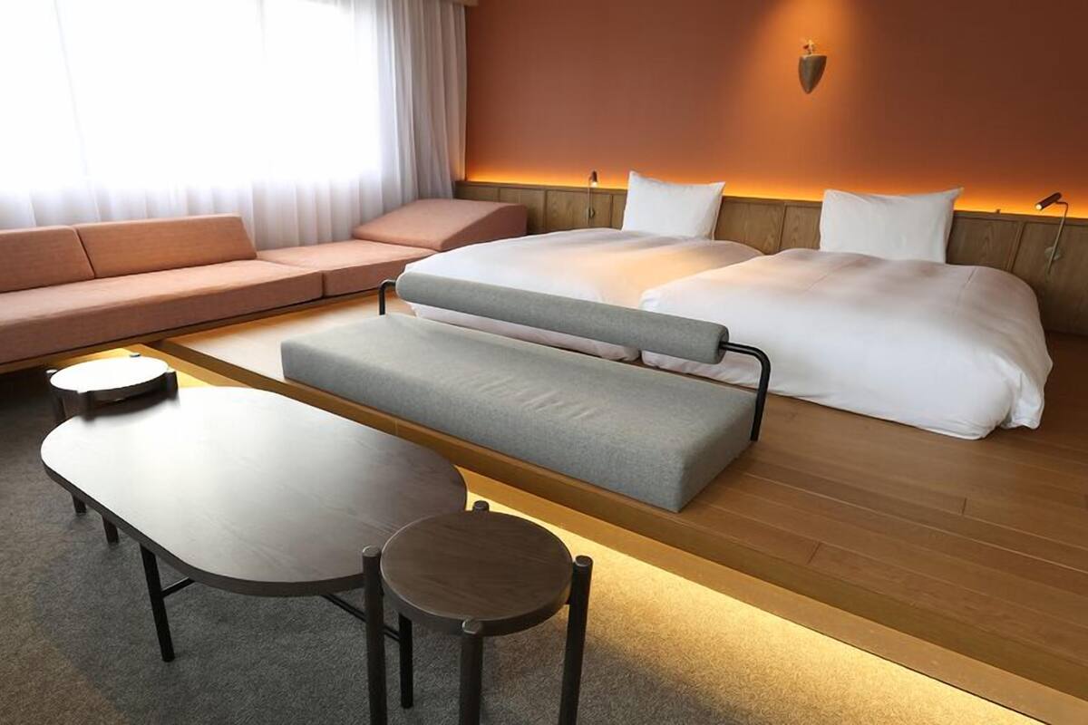 Een moderne hotelkamer met een bank, bed, houten bankje en een klein tafeltje.