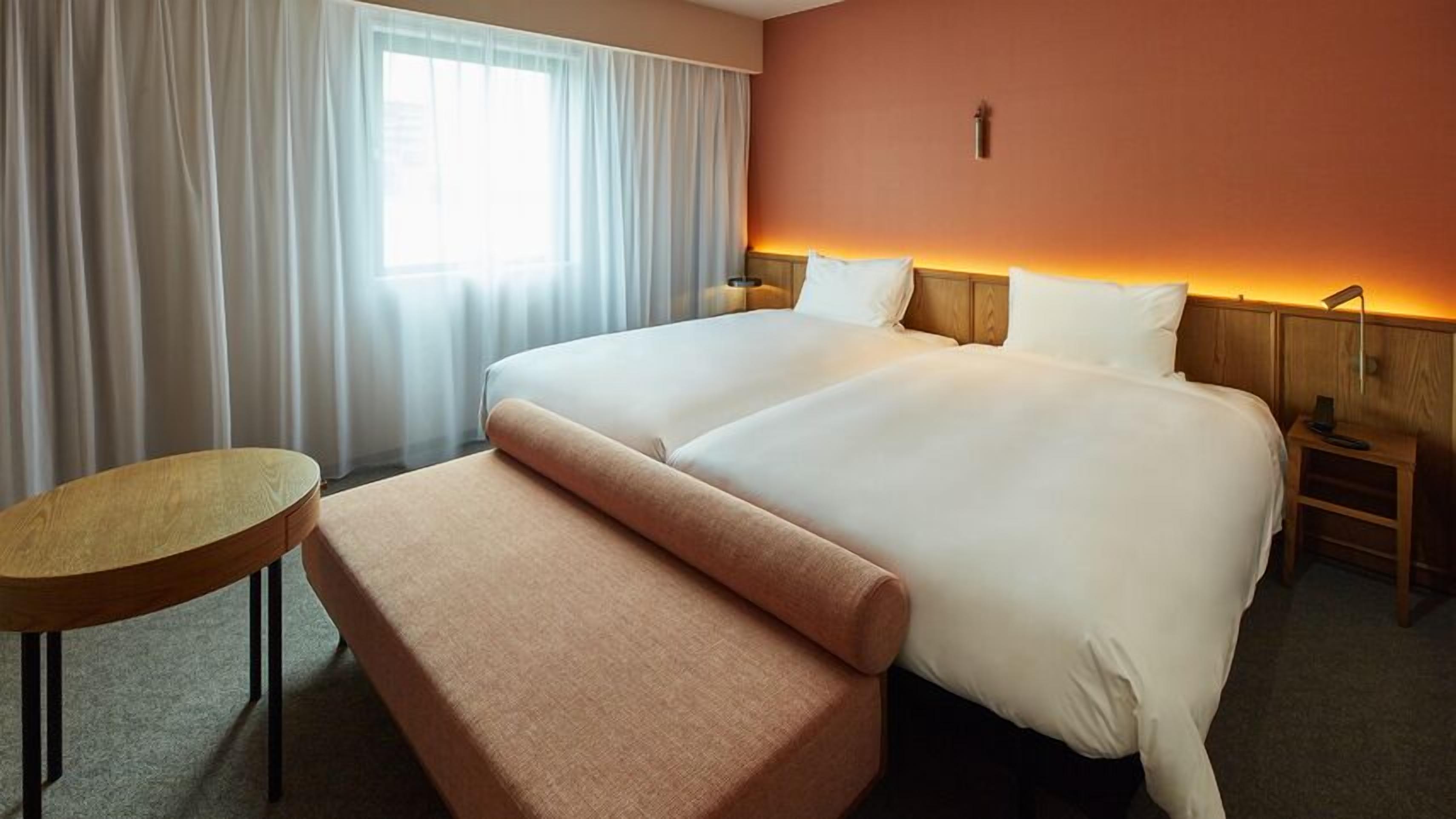 Une chambre d’hôtel avec un lit double, une petite table ronde, un banc et une table de chevet avec une lampe.