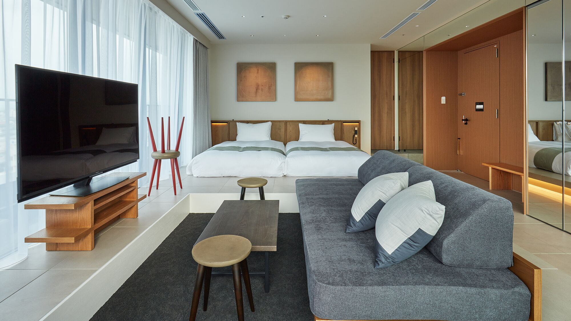 Une chambre d’hôtel moderne équipée d’un grand téléviseur à écran plat, d’un canapé, d’une petite table, d’un lit avec deux oreillers et d’une armoire.