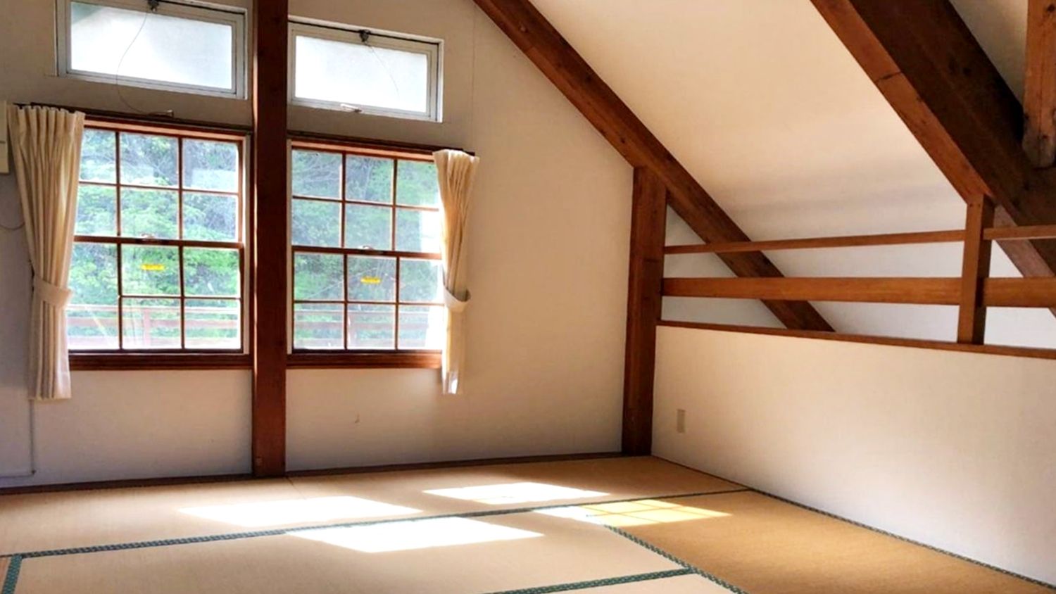 A room with tatami flooring, wooden beams, and large windows with curtains.