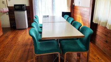 A dining area with a long table and six teal chairs, a small refrigerator, and a microwave on the left.