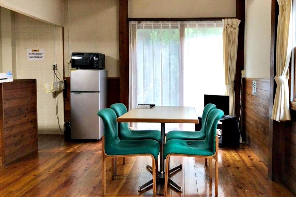 A compact kitchen with a refrigerator, a microwave, and a dining table with four chairs.