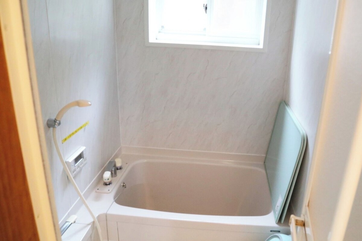 A small bathroom with a bathtub, a window, and a shower.