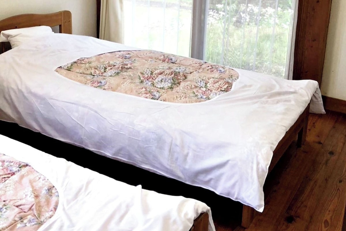 A bedroom with a bed covered in white sheets and a floral duvet.