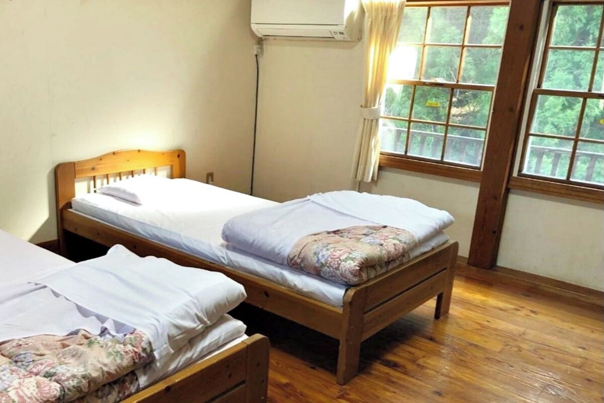 A room with two wooden beds, a window with curtains, and an air conditioning unit on the wall.