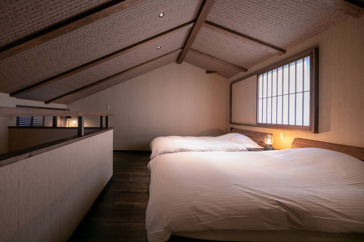 Ein Schlafzimmer mit schrägemausertem Dach, einem großen Fenster und einem Bett mit Nachttischlampe.