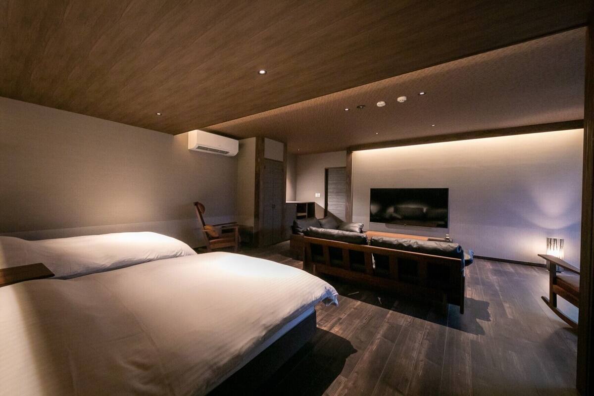 Ein modernes Schlafzimmer mit zwei Betten, einer Sitzecke, einem Fernseher und einer Holzbeschichtung an der Decke.