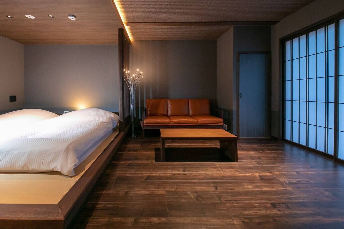 Ein modernes Hotelzimmer mit einem großen Bett, einer Couch, einem Couchtisch und Blick durch einen Shoji-Bildschirm.
