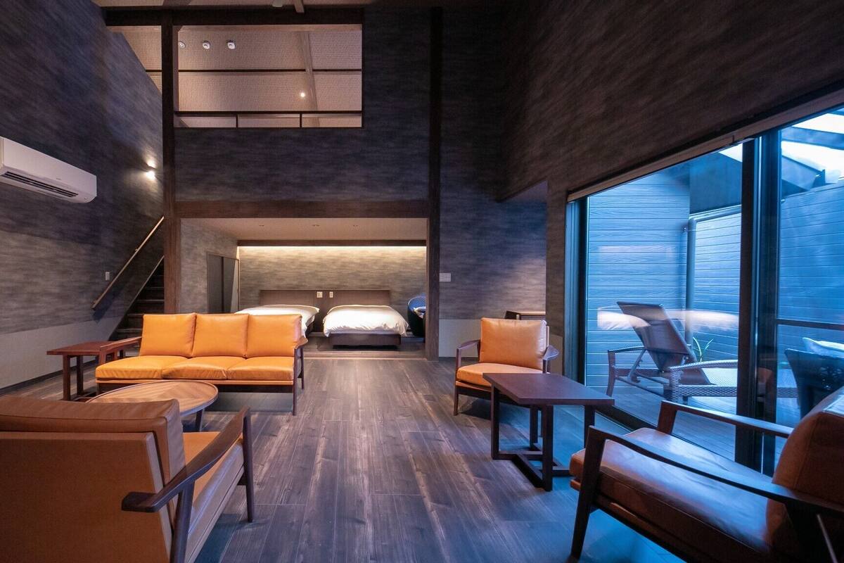 Ein modernes Hotelzimmer mit einer Couch, Sesseln, einem Fernseher, einem Bett und einem großen Fenster.
