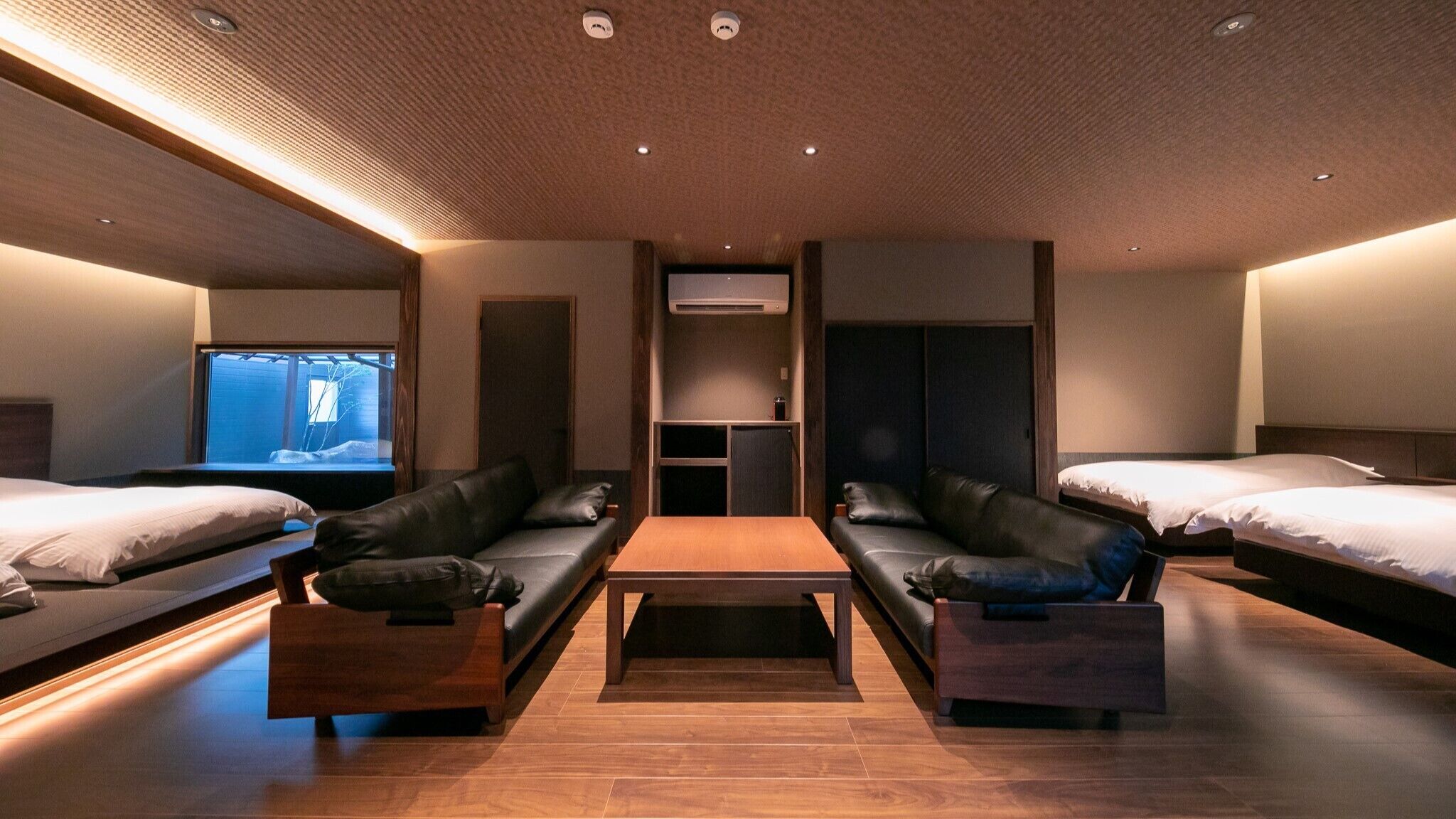 Hotellihuone, jossa on sohva, sohvapöytä, televisio ja kaksi sänkyä.