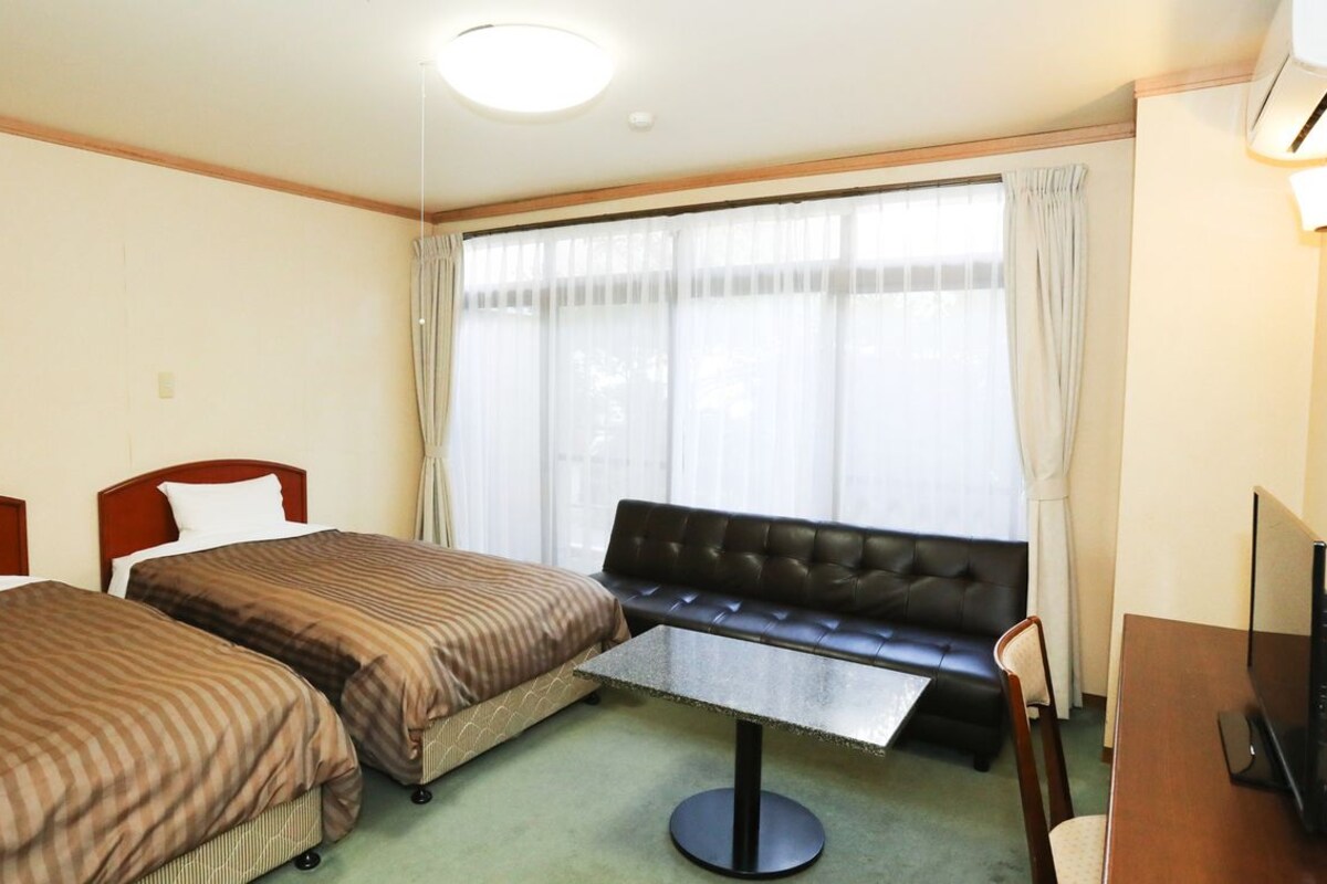 Una habitación de hotel con dos camas individuales, un sofá, una mesita y un televisor.