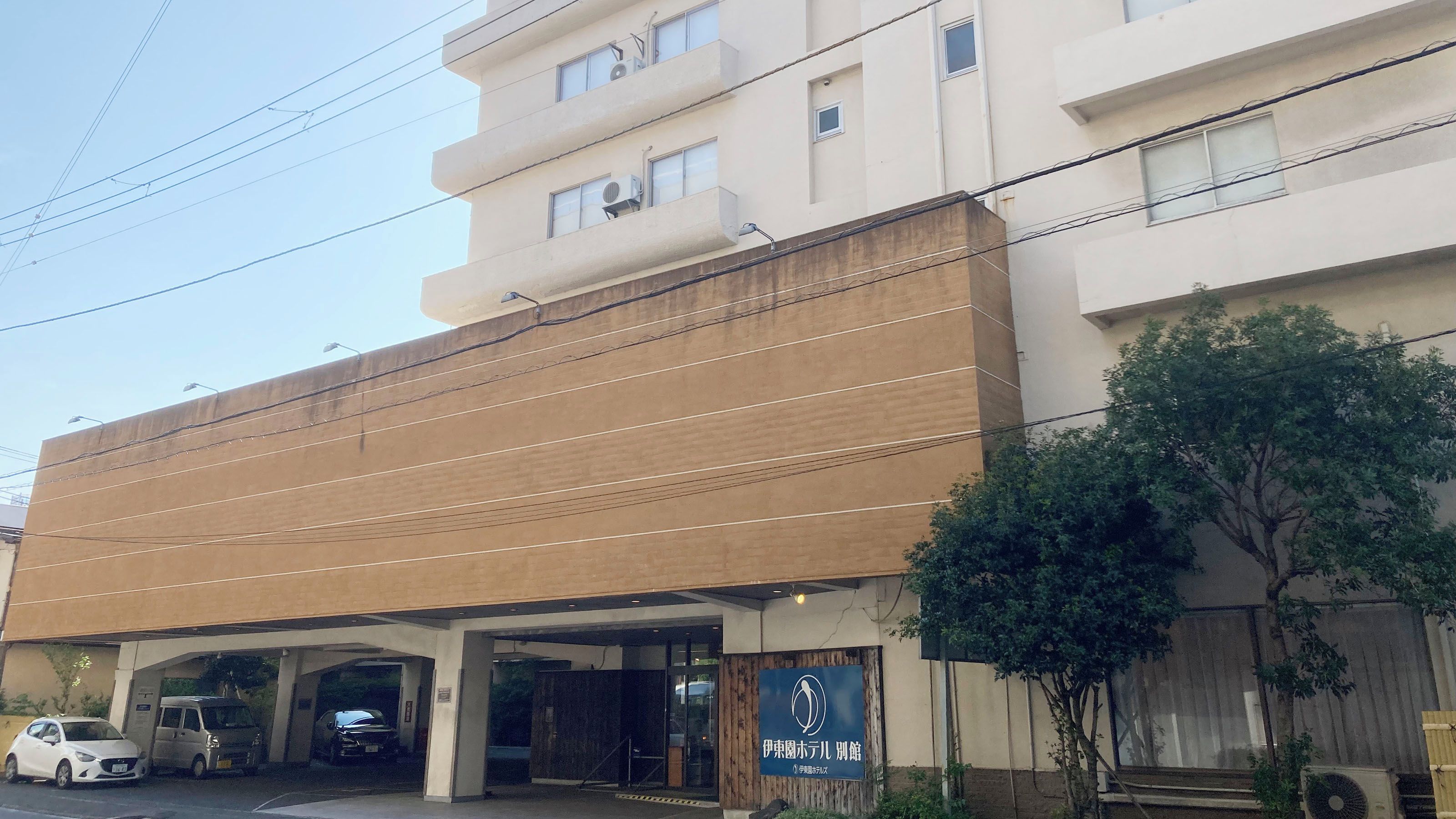 Un immeuble à plusieurs étages doté d’une façade plate, d’une entrée couverte où une voiture est garée, et d’une enseigne indiquant qu’il s’agit d’un hôtel.
