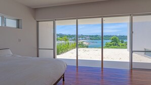 Een slaapkamer met een groot bed en een schuifpui naar een balkon met uitzicht op het strand.