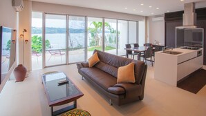 Een moderne woonkamer met een bank, een glazen salontafel en uitzicht op een balkon met tuinmeubilair.