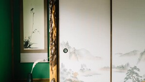 Une pièce de style japonais traditionnel, avec une porte coulissante en papier de riz (shoji), un rouleau suspendu et un vase orné d’une plume.