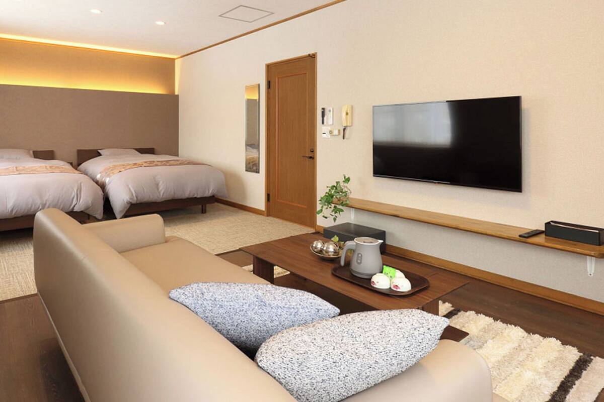 Een hotelkamer met twee bedden, een bank, een bijzettafeltje, een televisie en een kleine plant.