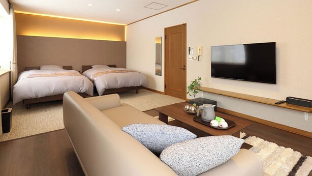 Une chambre d’hôtel avec deux lits, un canapé, une table basse, une télévision et une petite plante.