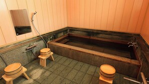 A traditional Japanese-style bathroom with a large soaking tub, two wooden stools, and a small wooden cabinet.