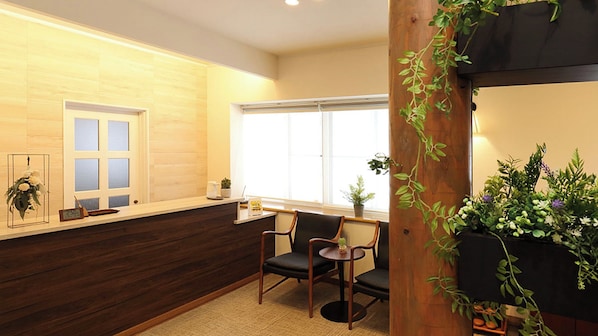 A reception area with a wooden reception desk, a chair, a window with blinds, and a potted plant.