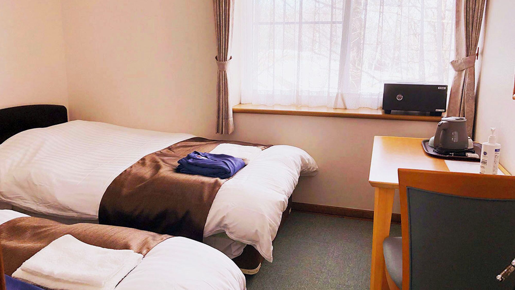 Una habitación de hotel con dos camas, un escritorio con una computadora portátil y una ventana con cortinas.
