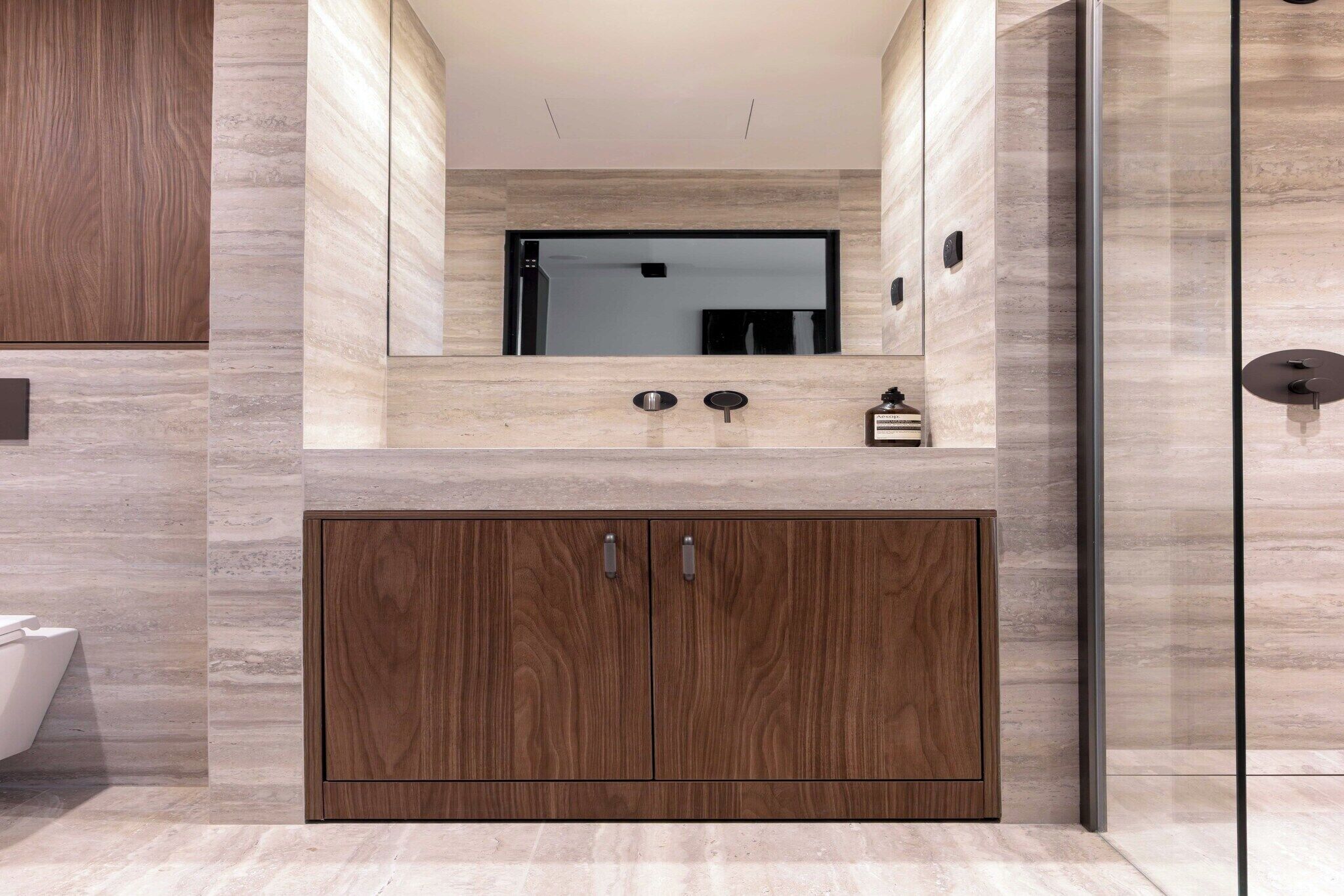 Een moderne badkamer met een houten wastafelmeubel, een spiegel en een klein wastafeltje.