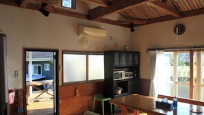 A wooden interior with a dining table, a green chair, a microwave, and a window with curtains. - Diving & Pension Riki (Setouchi)