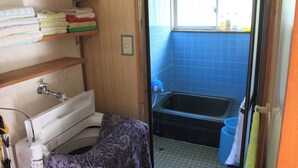 A compact bathroom with a bathtub, a window, and shelves with towels. - Diving & Pension Riki (Setouchi)