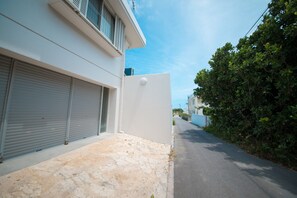 A narrow street with a white building on the left, closed shutters, and a stone-paved area. - Seaside Tellme <ishigakijima> (Ishigaki)