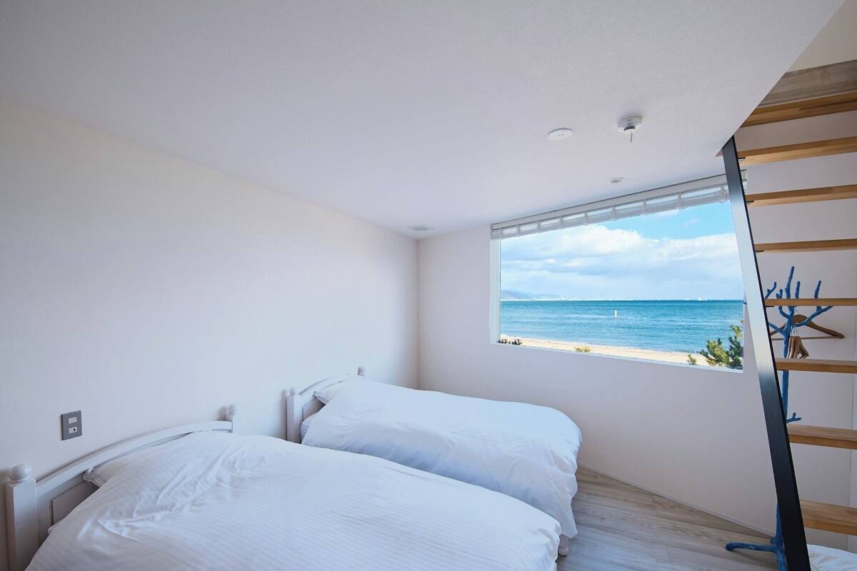 Une chambre avec deux lits, une fenêtre donnant sur la mer et un escalier en bois.