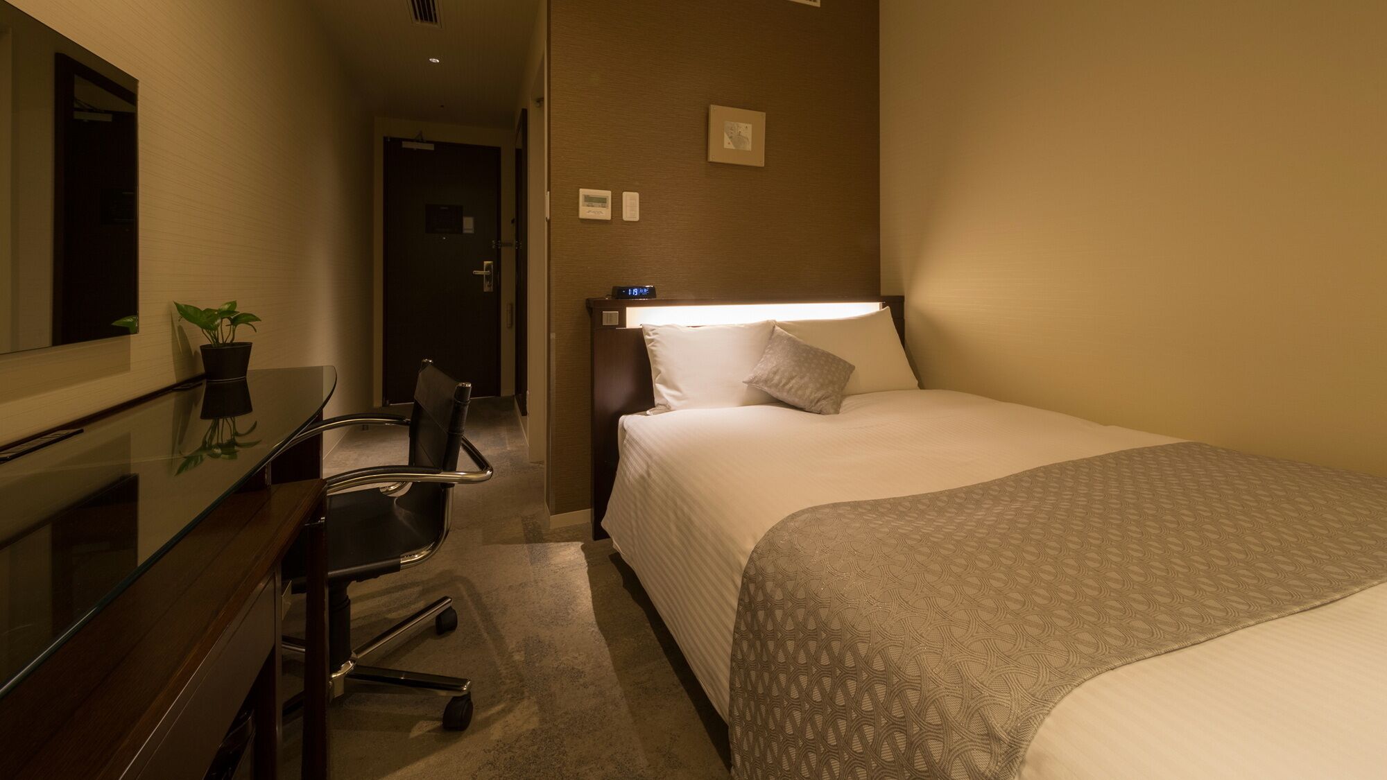 Ein Hotelzimmer mit einem Bett, einem Schreibtisch, einem Stuhl, einem Spiegel und einer Wanduhr.