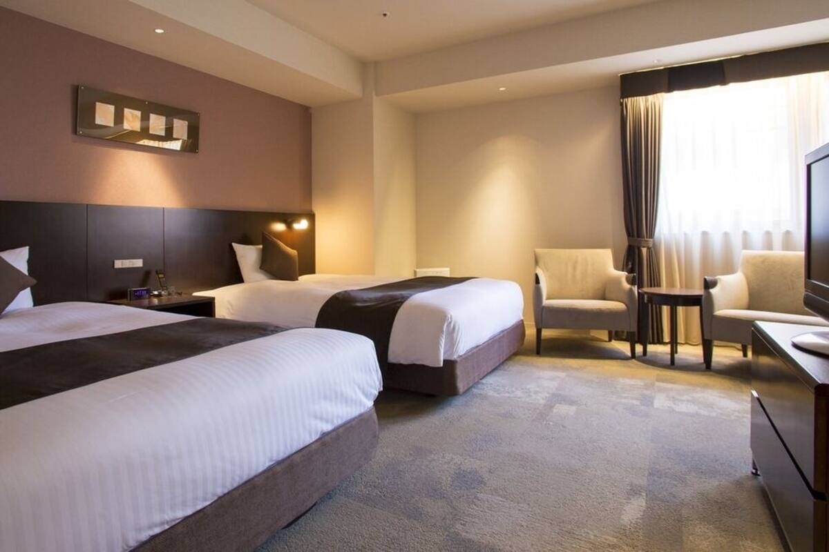 A hotel room with two beds, a desk, a chair, and a television.