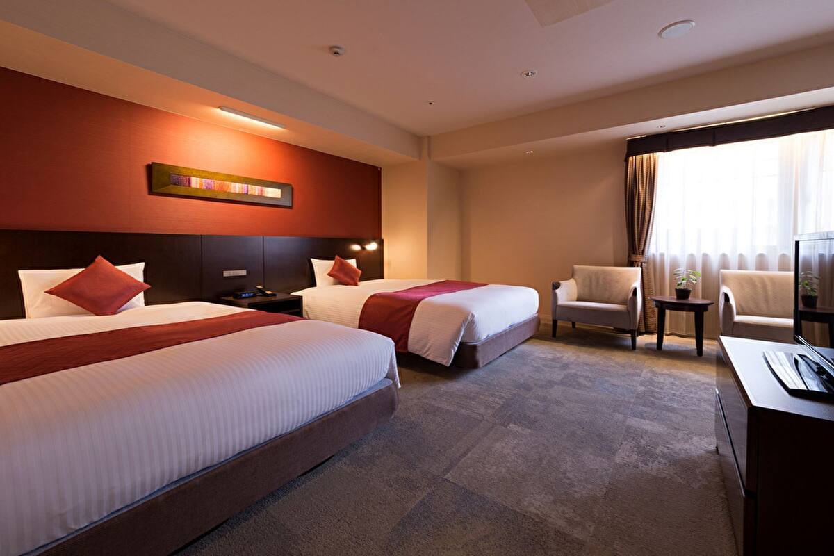 A hotel room with two beds, a desk with a TV, a chair, and a window with curtains.