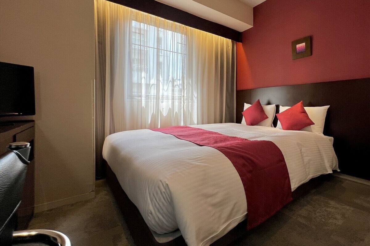 A hotel room with a large bed, a TV, a desk, and a window with curtains.
