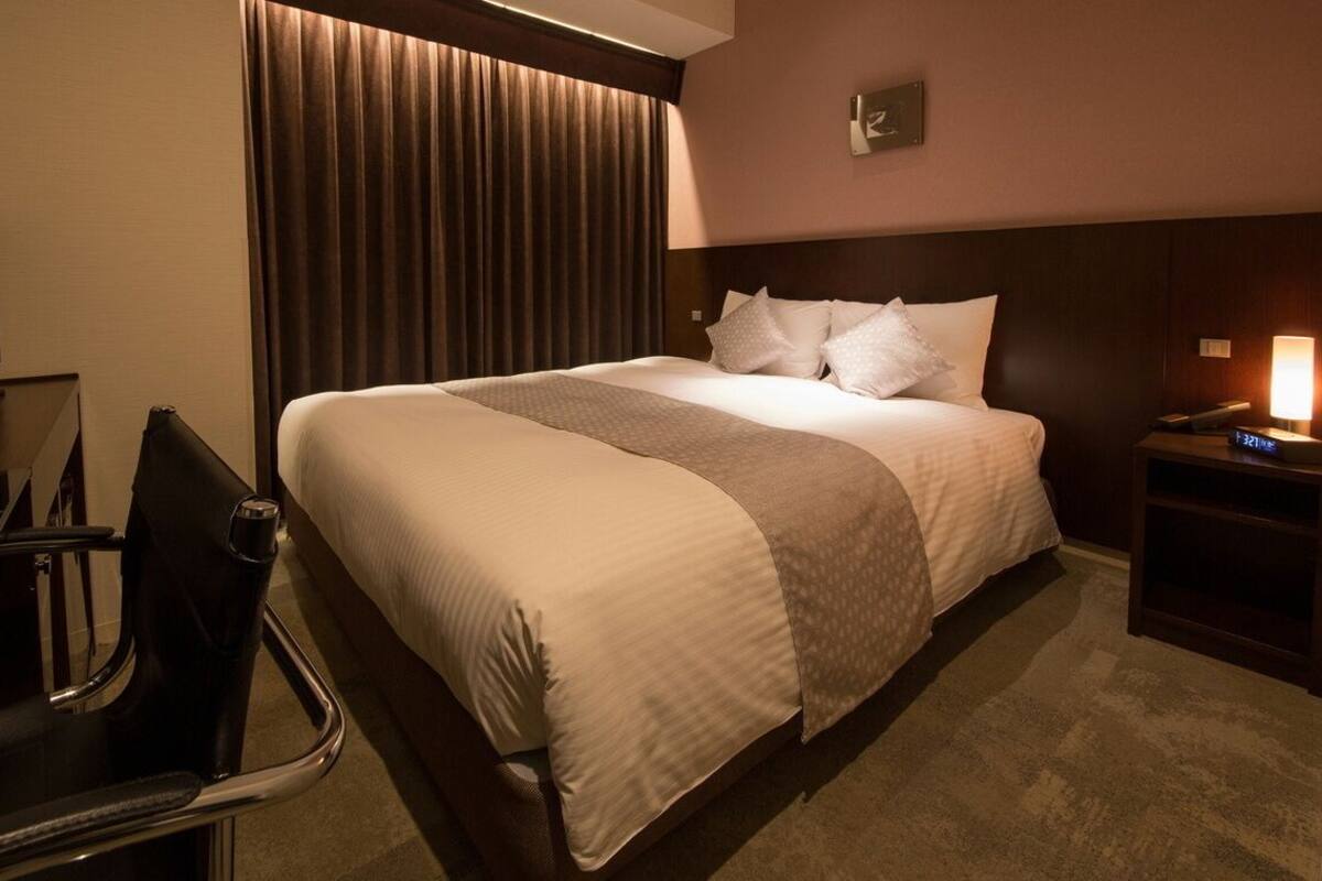 A hotel room with a bed, a TV, a desk, and a chair.