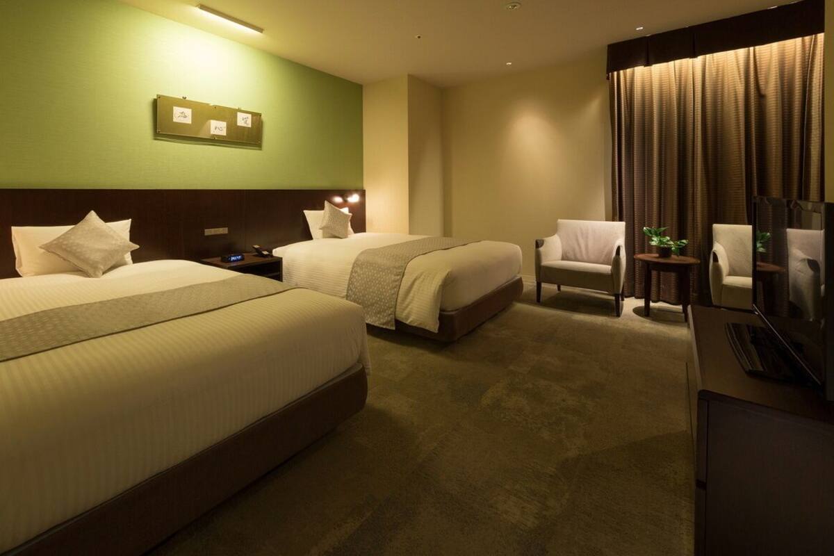 A hotel room with two beds, a desk, a chair, a television, and a small table with a plant.