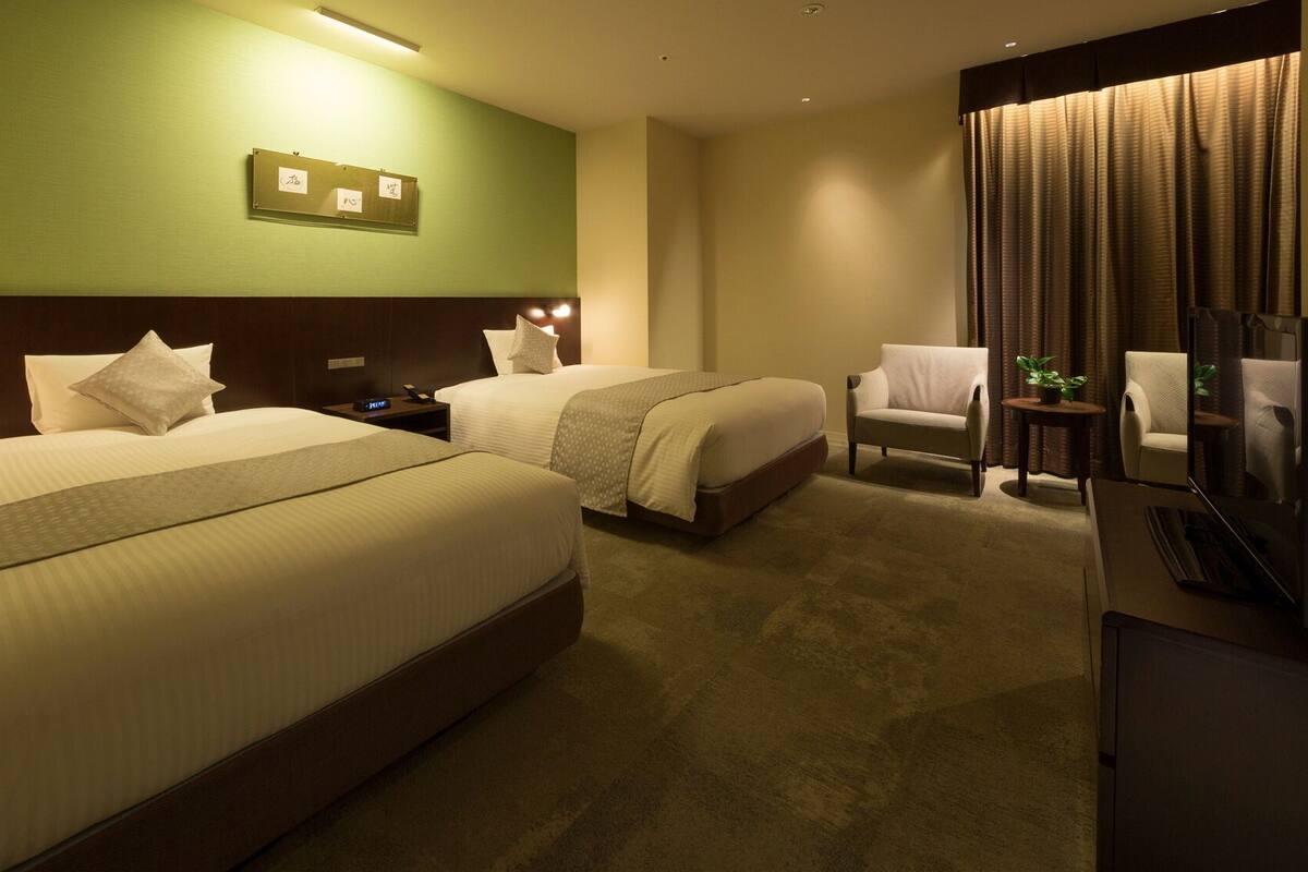 A hotel room with two beds, a chair, a desk with a computer, and a television.