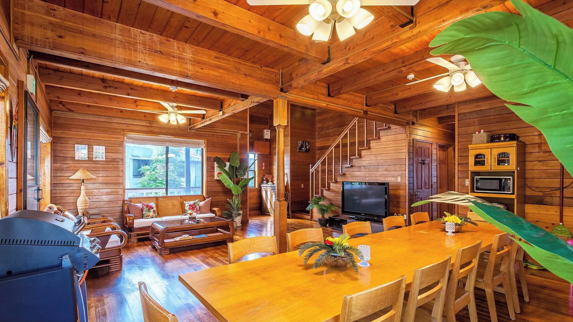 Interior de una cabaña de madera con comedor, asientos, televisor y escalera.
