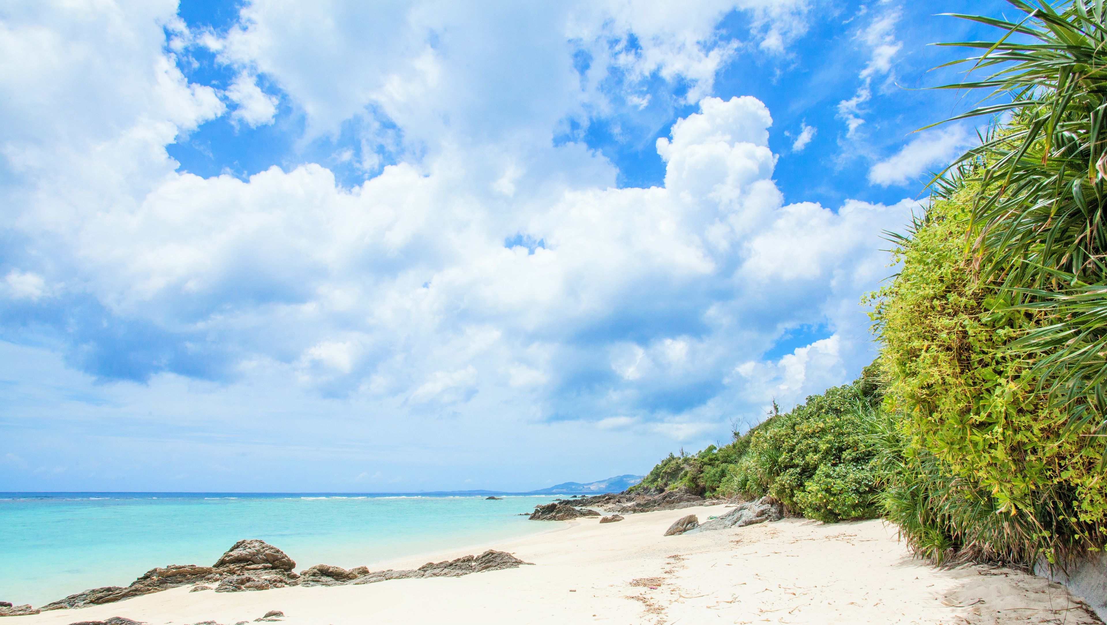 A beach with clear turquoise water, white sand, and a rocky shoreline.