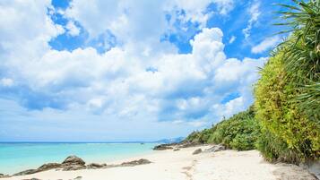 A beach with clear turquoise water, white sand, and a rocky shoreline.