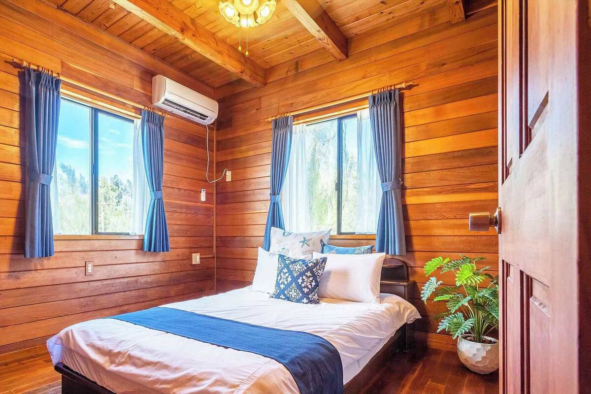A wooden cabin bedroom with a bed, curtains, an air conditioning unit, and a window.