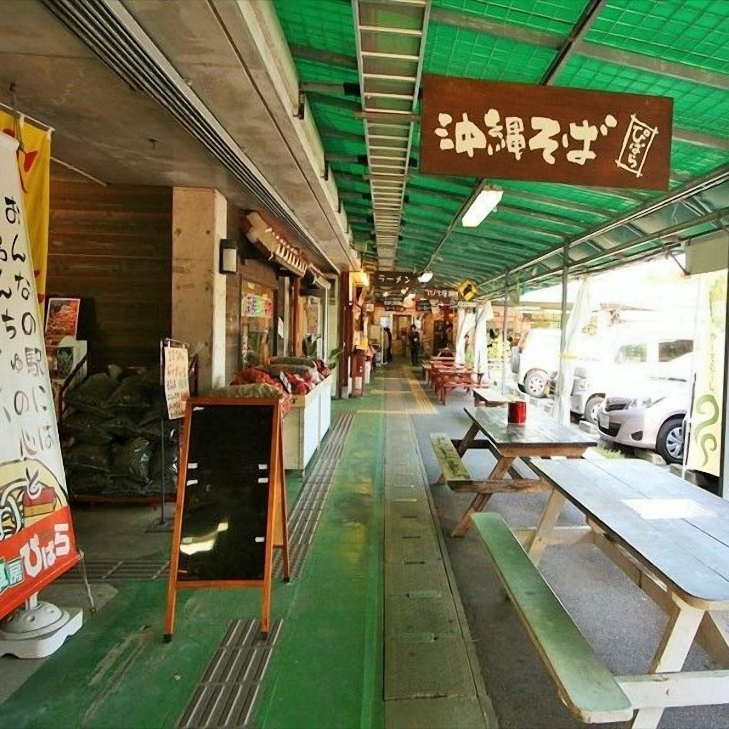 A covered outdoor food market with tables and benches, signs in a foreign language, and a green ceiling.
