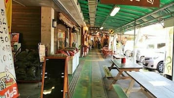 Un mercado de comida al aire libre con techado, mesas, bancos, letreros en un idioma extranjero y techo verde.